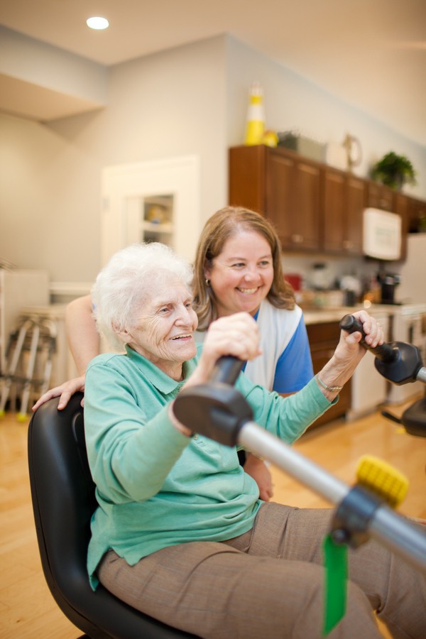 An elderly woman exercising with the support of a caregiver.