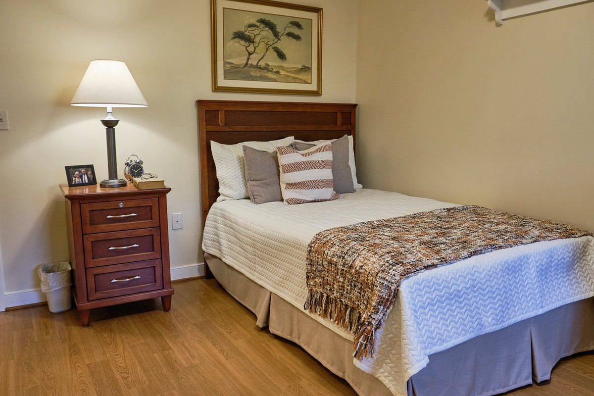 A cozy bedroom with a neatly made bed, nightstand, and lamp.
