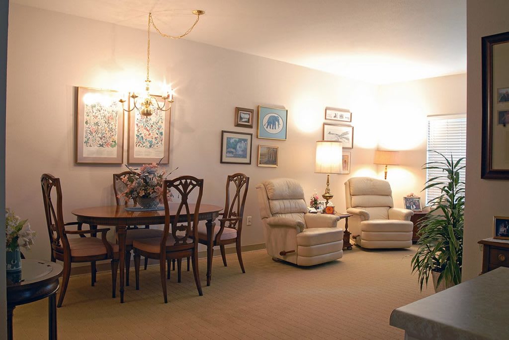 A cozy living room with a dining area, featuring comfortable chairs, a dining table, lamps, and decorative wall art.