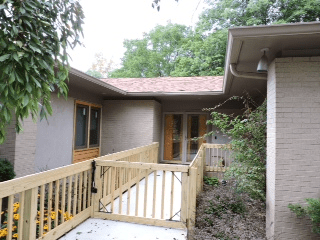 A house exterior with a wooden ramp surrounded by trees.