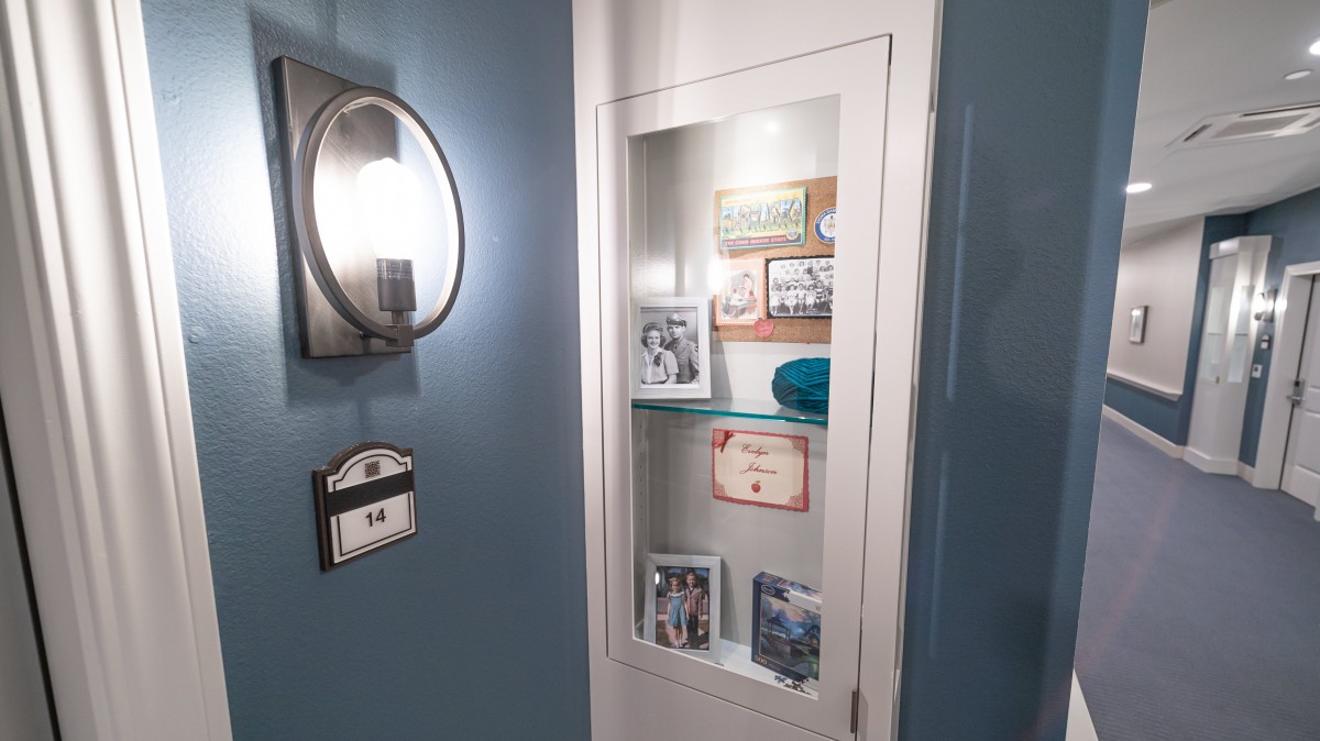 A cozy wall display featuring photographs and memorabilia, accompanied by a round mirror and light fixture.