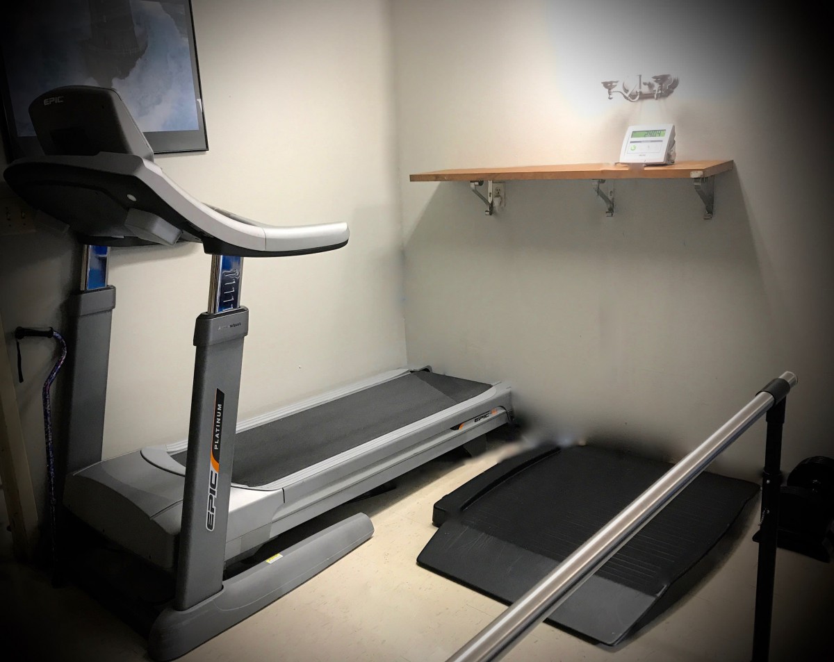 A minimalist fitness room featuring a treadmill and a small shelf.