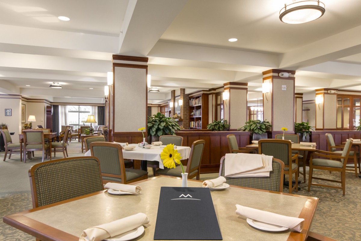 A well-lit dining area with neatly set tables and chairs, featuring elegant decor and modern lighting.