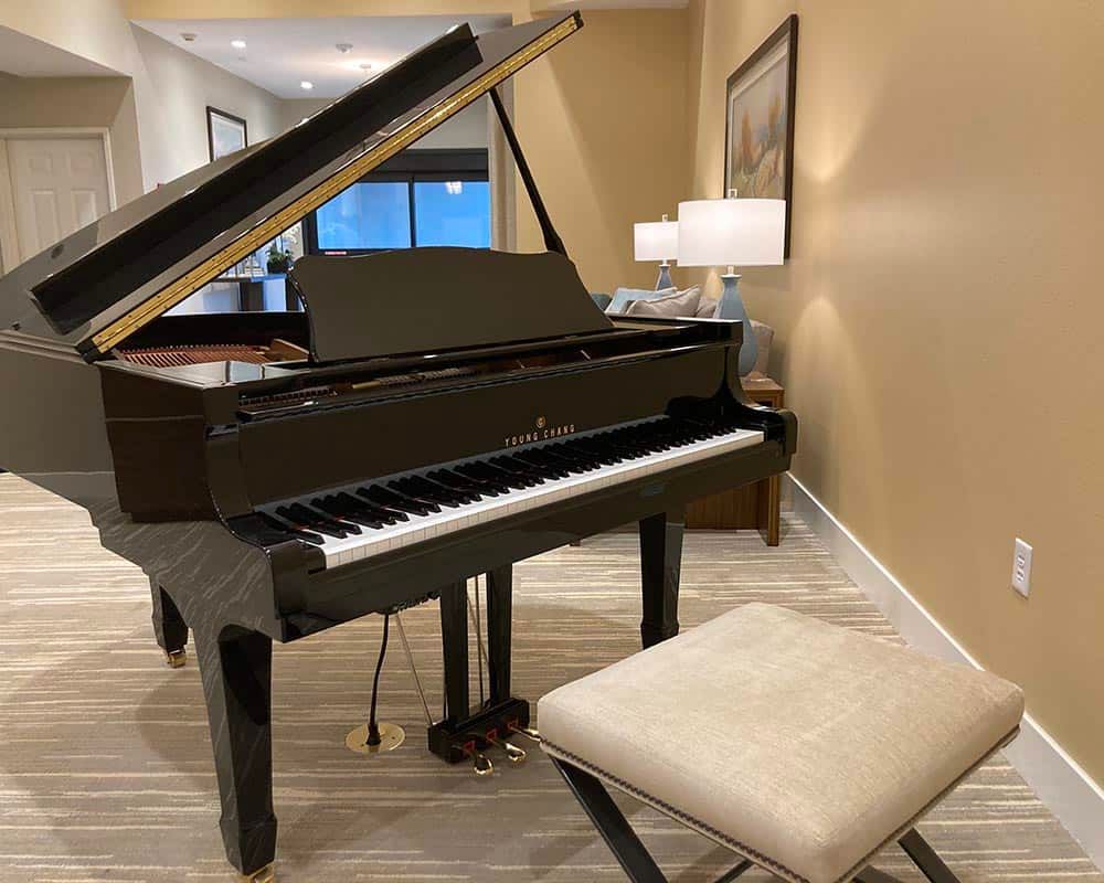 A grand piano placed in a stylish living room setting, accompanied by a comfortable stool.