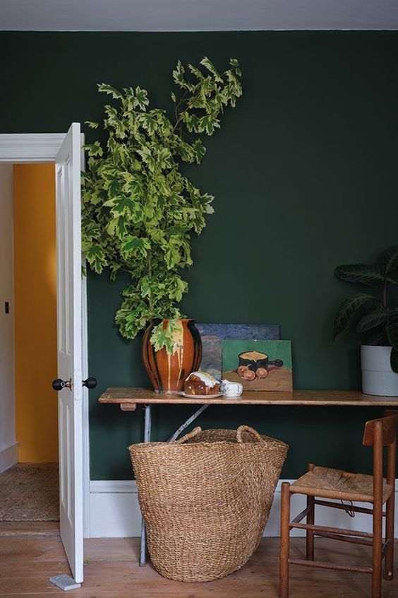 A cozy interior with a lush plant, wooden table, and artwork against a dark green wall.