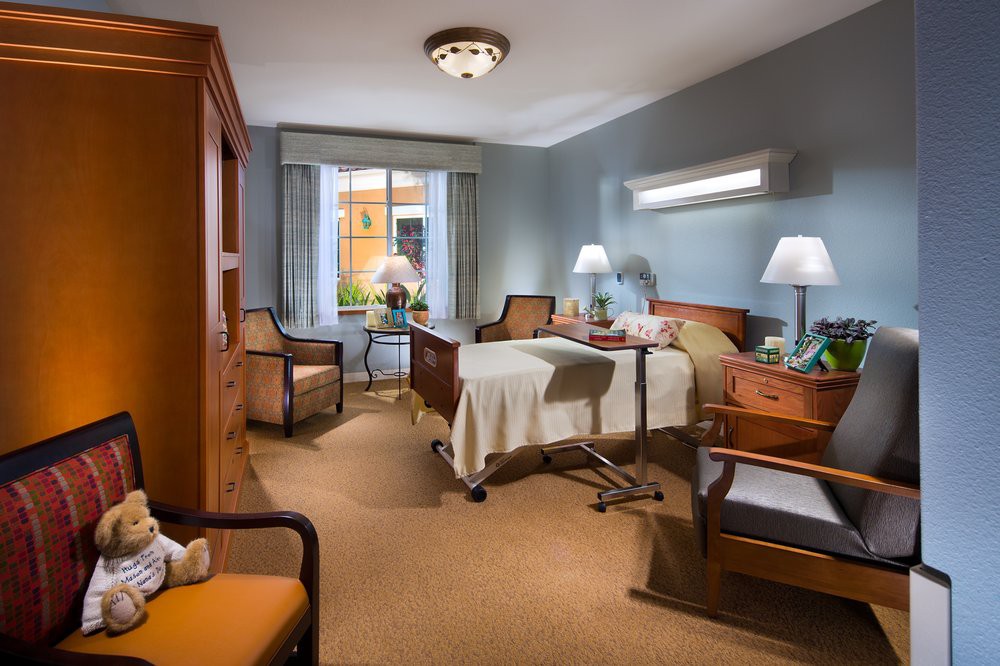 A well-furnished hospital room with a bed, chairs, and a window, providing a comfortable environment.