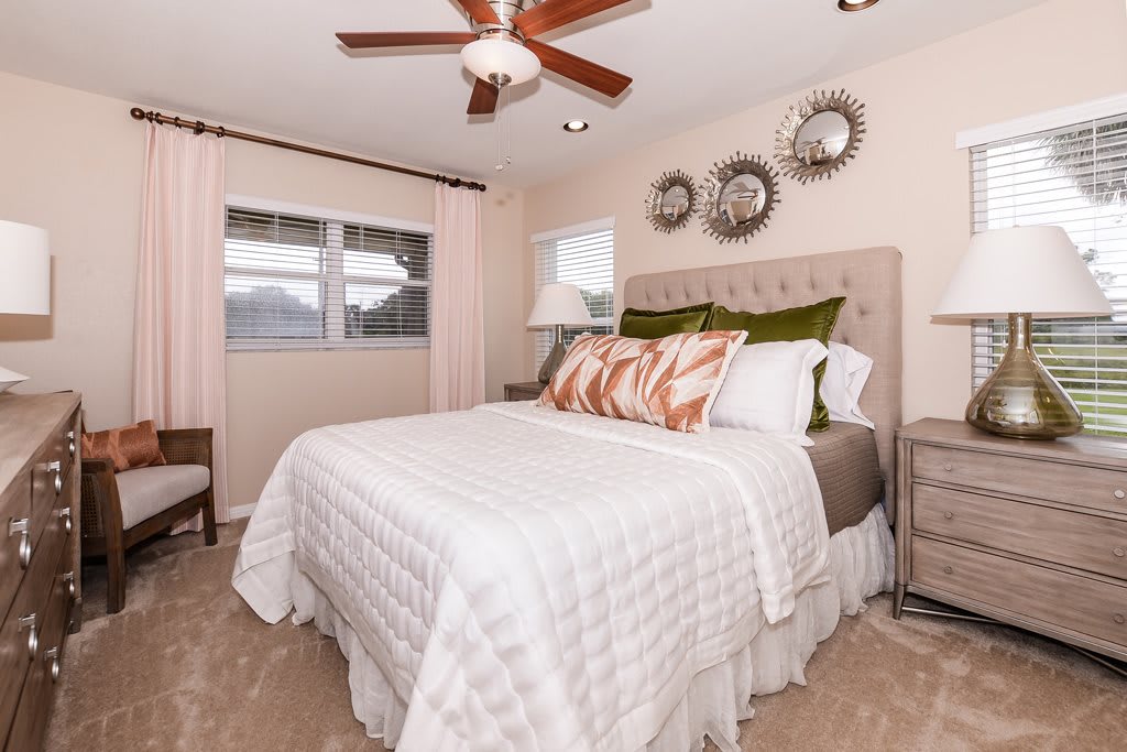 A cozy bedroom featuring a neatly made bed with decorative pillows, a ceiling fan, and artistic wall decorations.