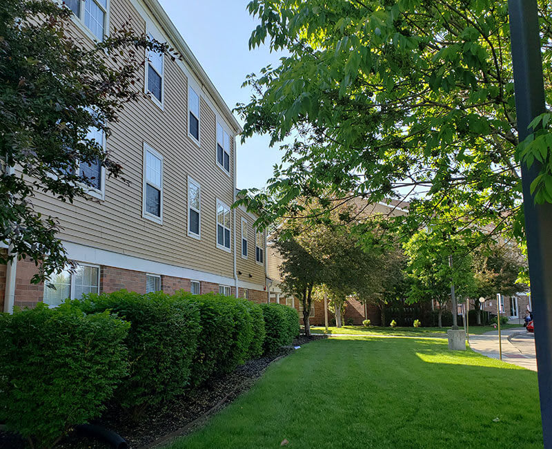 A quiet residential building surrounded by well-maintained greenery and a lush lawn on a sunny day.