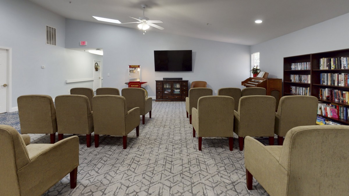 A well-lit room with rows of chairs facing a television mounted on the wall.