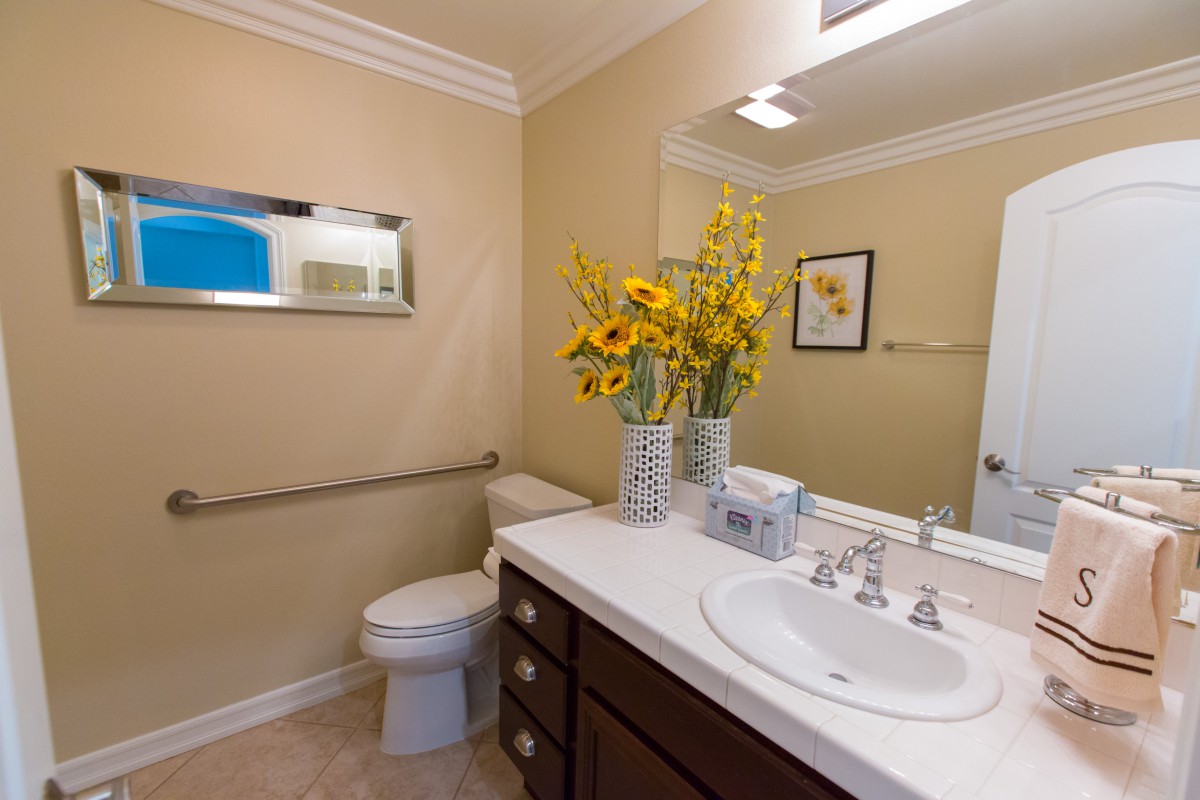 A well-lit bathroom with a countertop sink, mirror, toilet, and a vase of sunflowers.