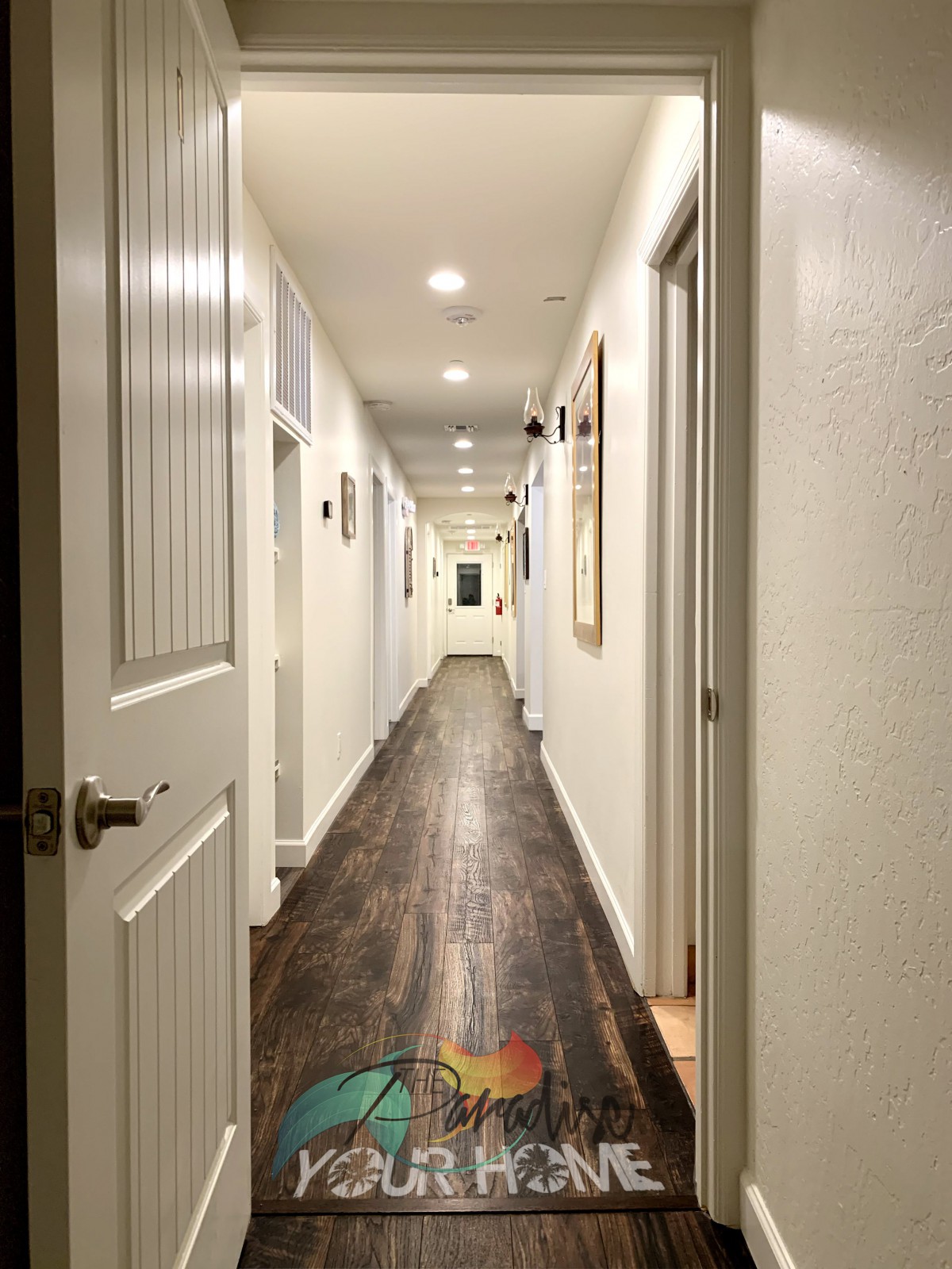 A long, well-lit hallway with wooden floors and open doors on each side.