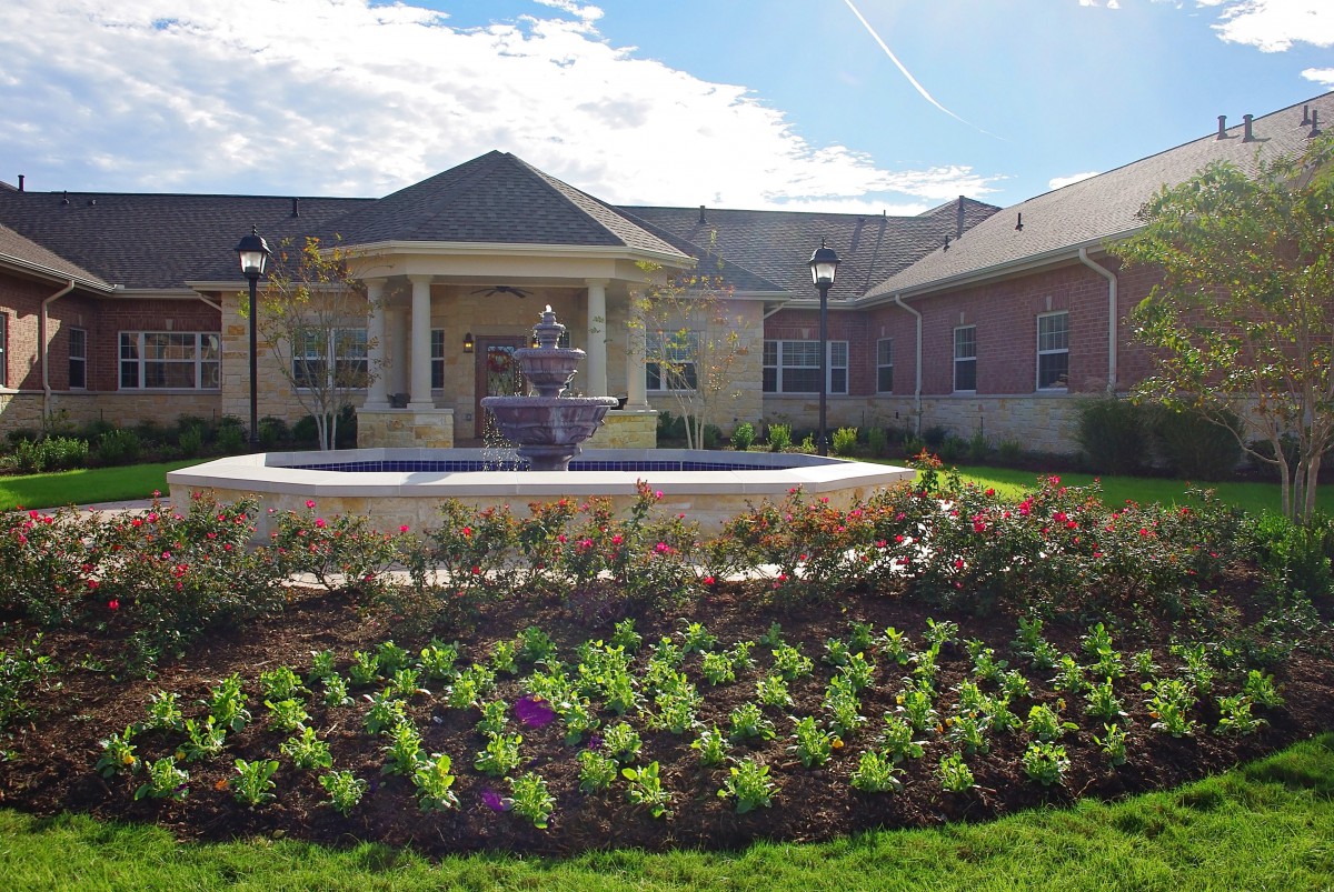 A well-maintained garden with a fountain in front of a large building.