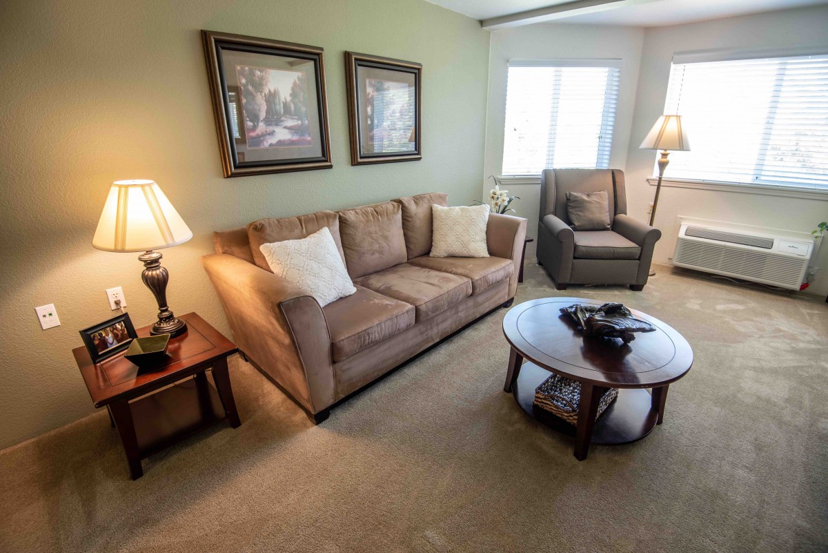 A cozy living room with a sofa, armchair, and coffee table, decorated with lamps and artwork on the walls.