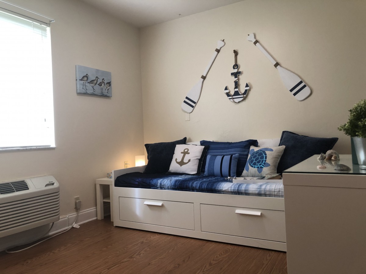 A cozy bedroom decorated with a nautical theme, featuring anchor and oar wall decor above a daybed adorned with blue and white pillows.