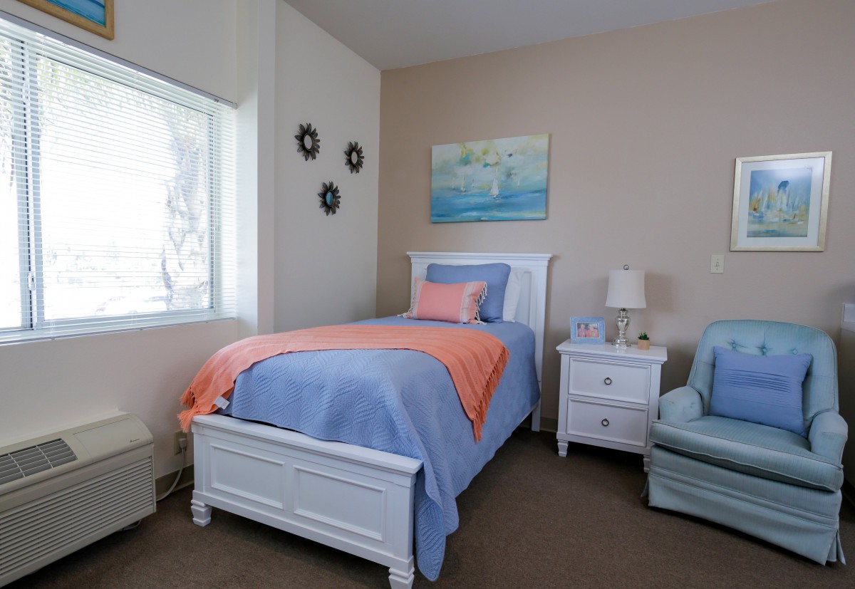 A cozy bedroom featuring a single bed with blue bedding and orange accents, complemented by a nightstand and armchair.