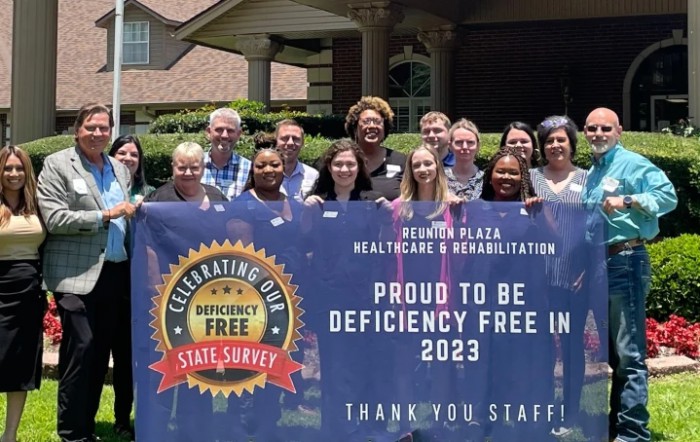 A group of healthcare staff celebrating a deficiency-free survey result in 2023, holding a banner outside.
