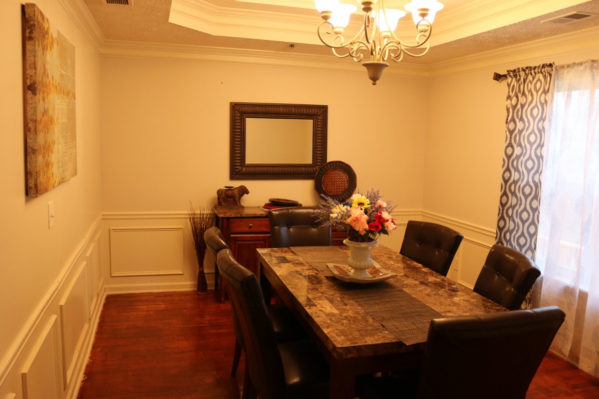 A warmly lit dining room with a large table and chairs, featuring a mirror and decorative elements.