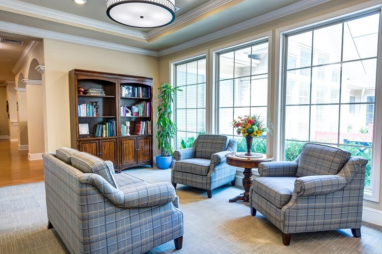 A cozy living room with armchairs and a bookcase by large windows.