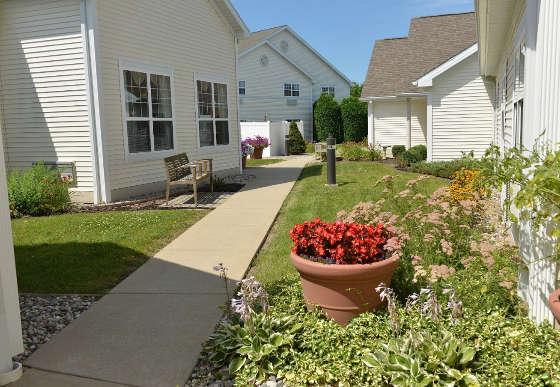 A peaceful residential pathway lined with potted flowers and garden spaces between white buildings.