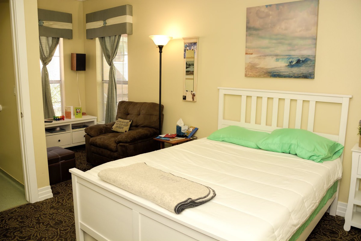A cozy bedroom with a bed, armchair, and floor lamp, enhanced by curtains and a wall painting.