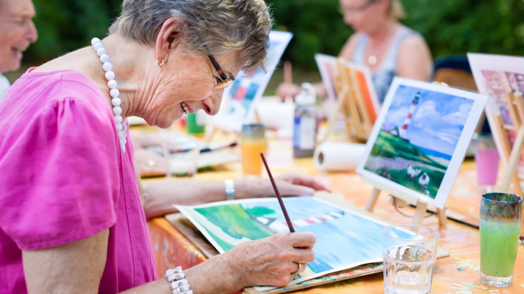 An elderly woman enjoys painting during an outdoor art class.