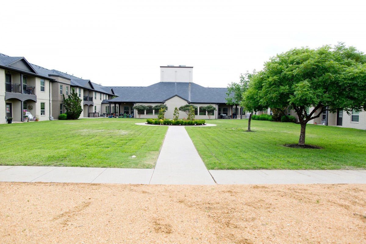 A well-maintained building with a large lawn and pathway leading to the entrance, surrounded by trees.