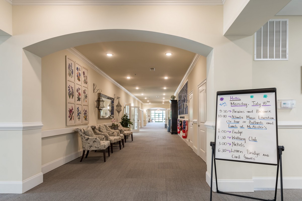 A well-lit hallway featuring a seating area, framed artwork on the walls, and a notice board.