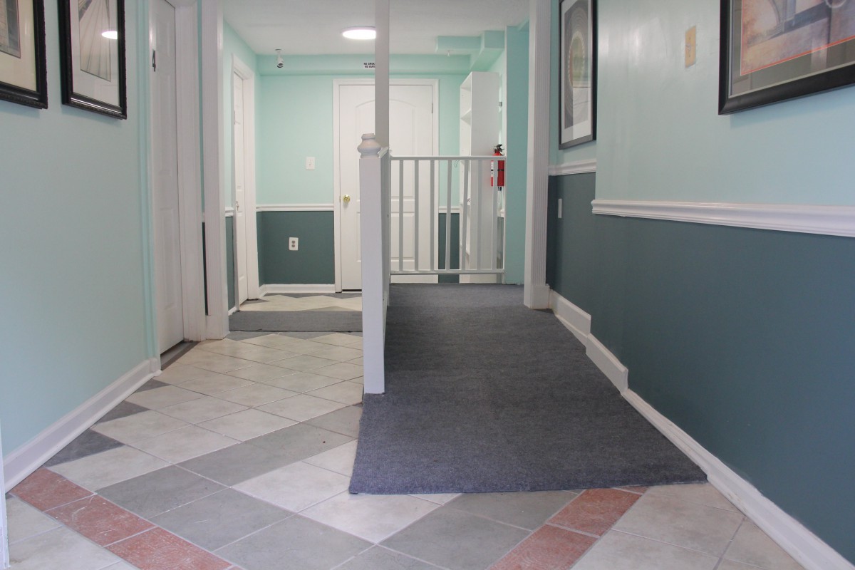 A hallway with a carpeted ramp leading to doors and a fire extinguisher on the wall.