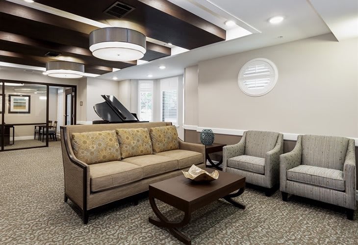 A modern living room featuring a sofa, chairs, coffee table, and a grand piano in the corner.