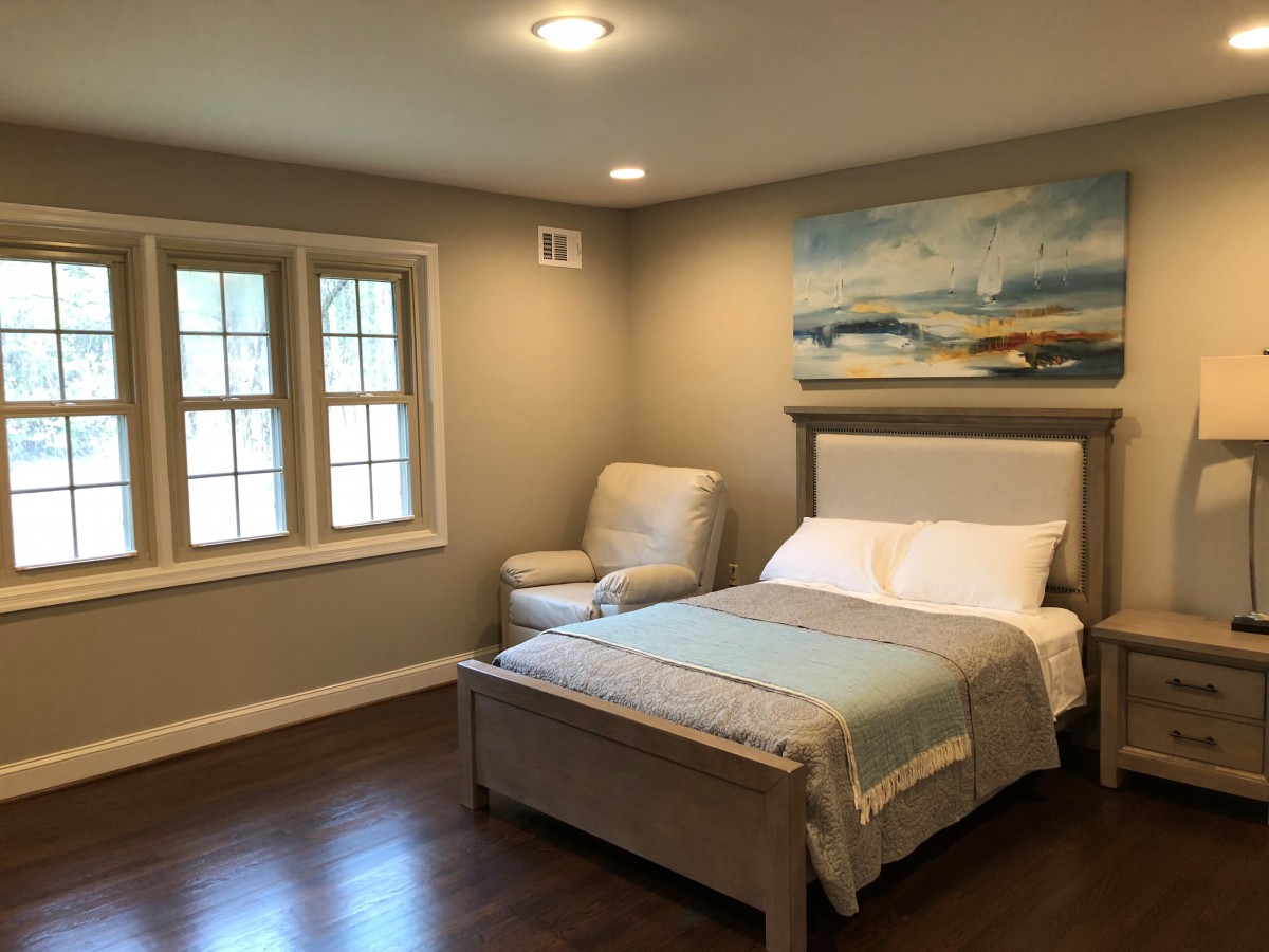 A cozy bedroom featuring a neatly made bed, an armchair by the window, and a piece of wall art above the headboard.