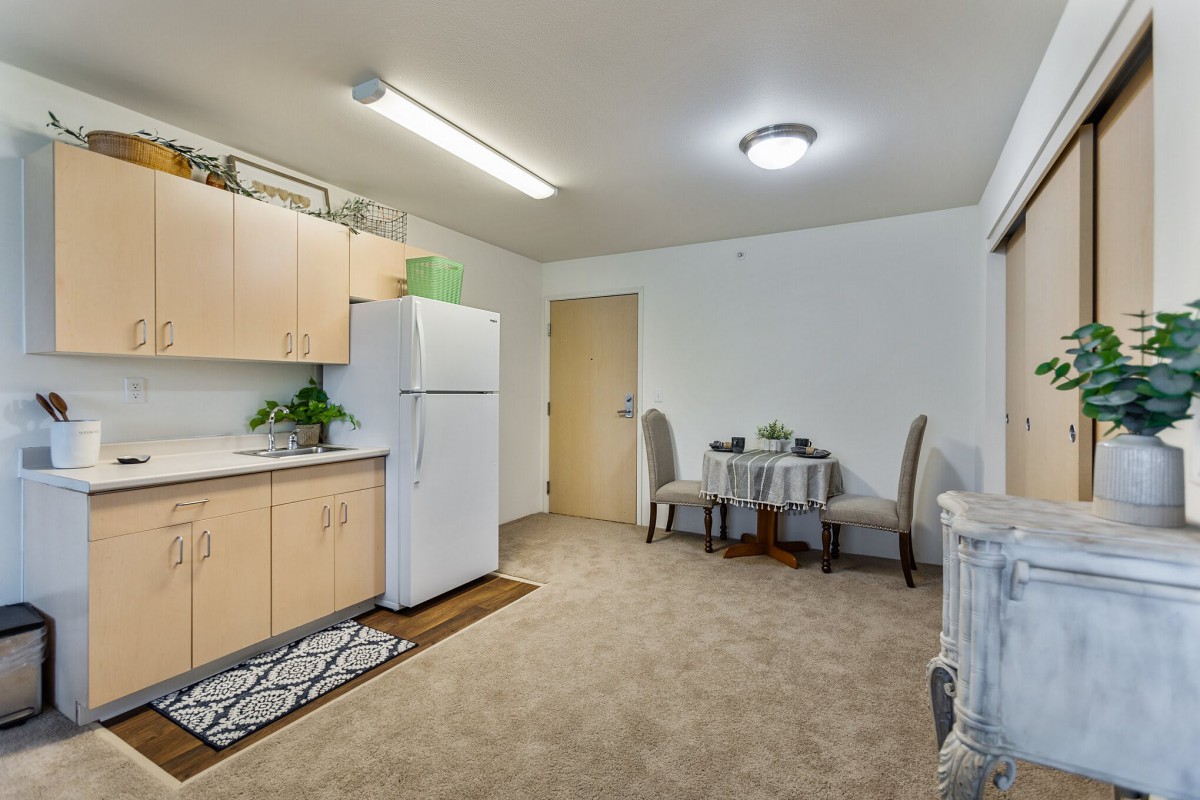 A cozy apartment kitchen and dining area with light wooden cabinets, a refrigerator, and a small dining table set.