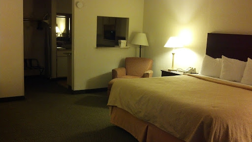 A cozy hotel room featuring a bed, lamp, and a comfortable chair.