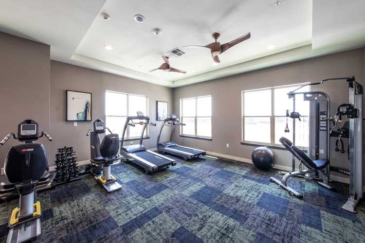 A well-lit fitness room with treadmills, exercise equipment, and weights.