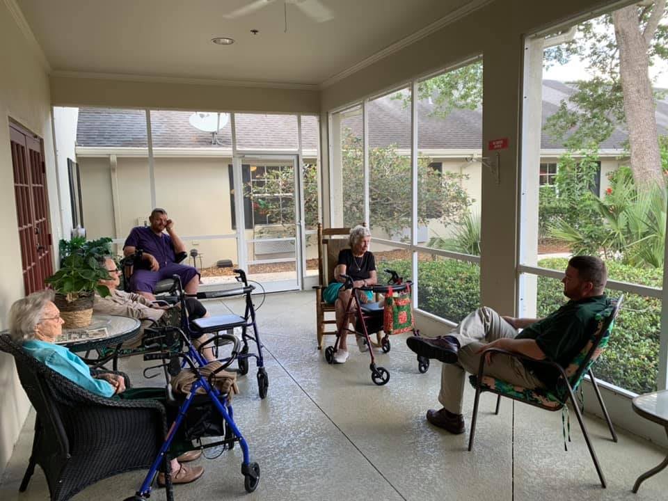 A group of people, some using wheelchairs, gather indoors for a conversation in a well-lit room.