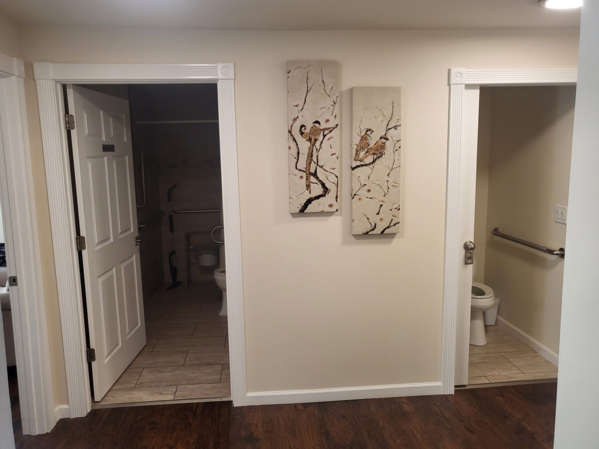 A hallway with two open doors leading to bathrooms and wall art between them.