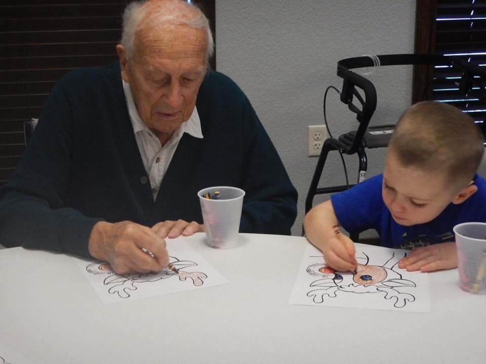 An elderly man and a young boy enjoy a coloring activity together.