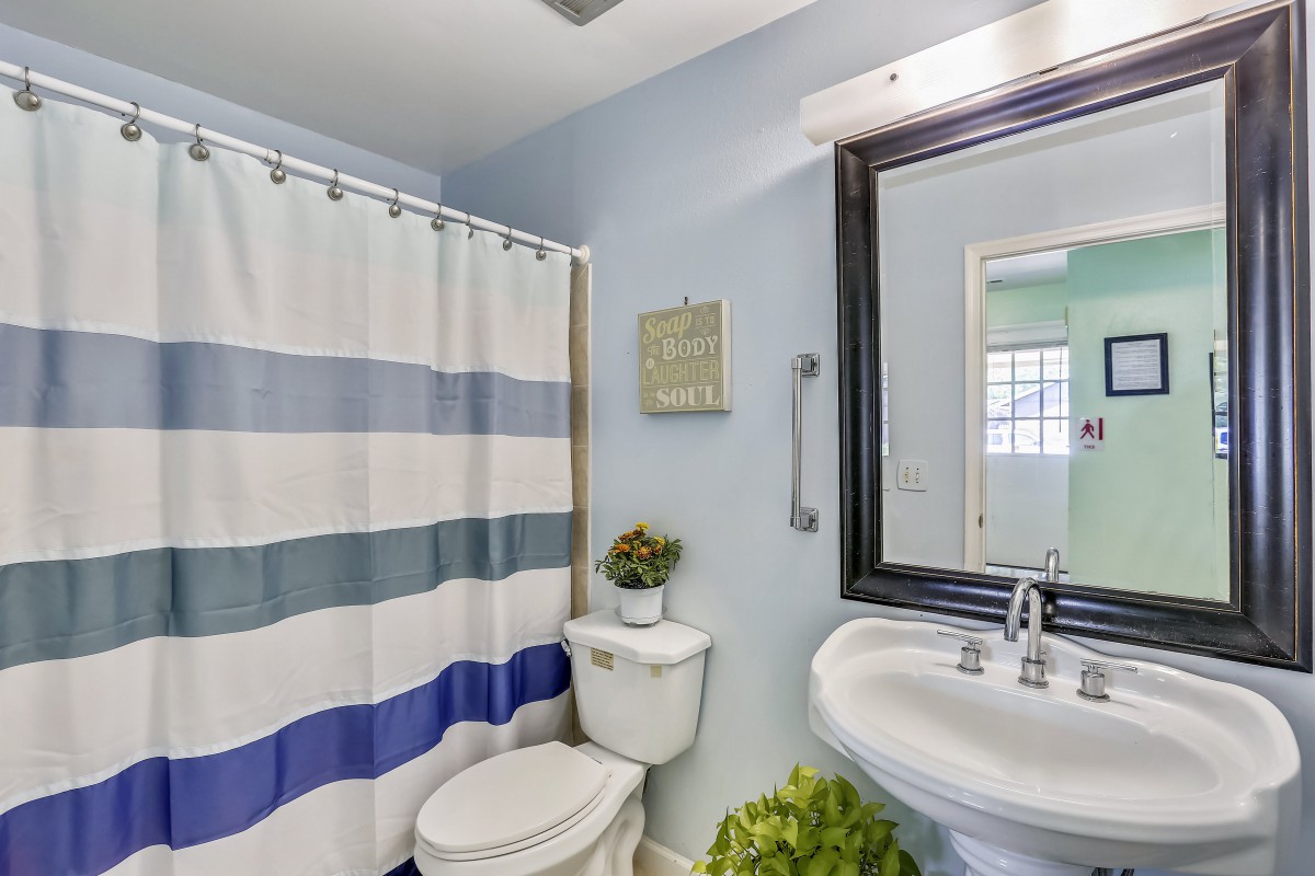 A clean and modern bathroom with a striped shower curtain, white toilet, pedestal sink, and decorative elements.