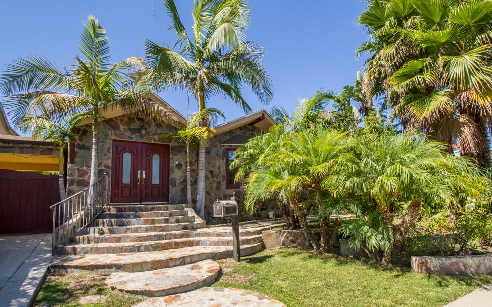 A tropical house surrounded by palm trees and lush greenery under a clear blue sky.
