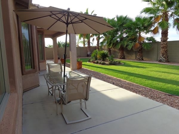 A sunny backyard patio with outdoor seating, umbrella, and a well-maintained garden.