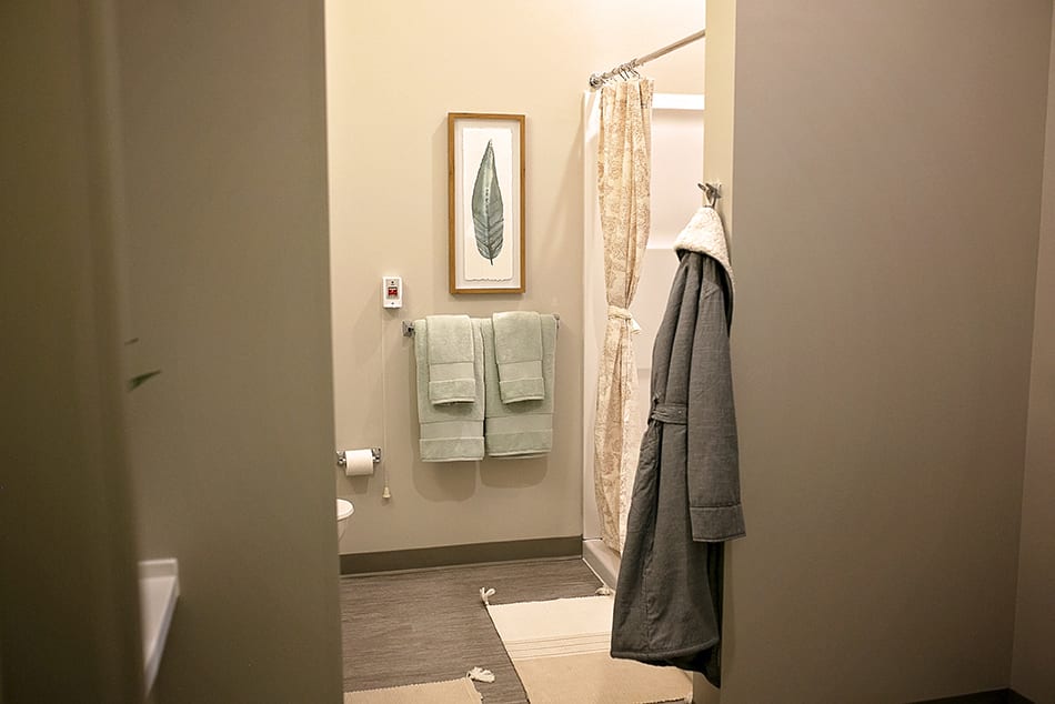 A bathroom interior featuring hanging towels, a robe, and framed artwork.