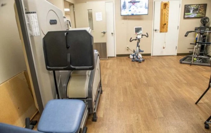 A gym room featuring exercise equipment, including an exercise bike and workout benches on a wooden floor.
