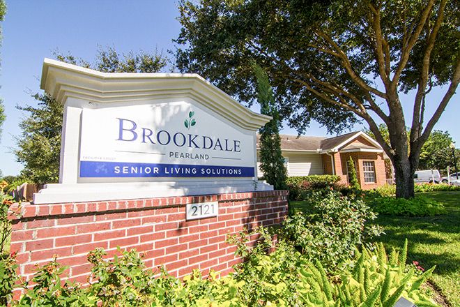 A sign for Brookdale Senior Living Solutions with surrounding landscaping and a building in the background.