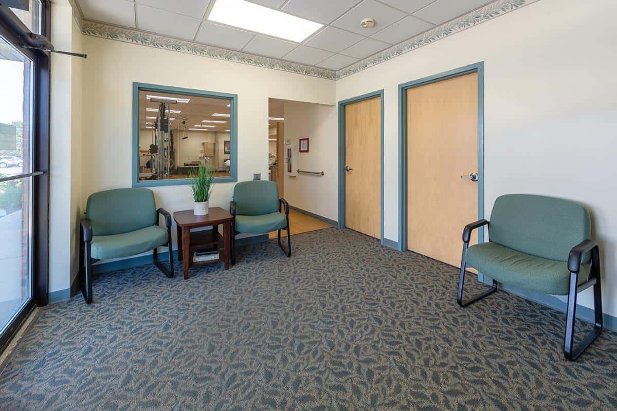 An empty waiting room with chairs and carpeted flooring.