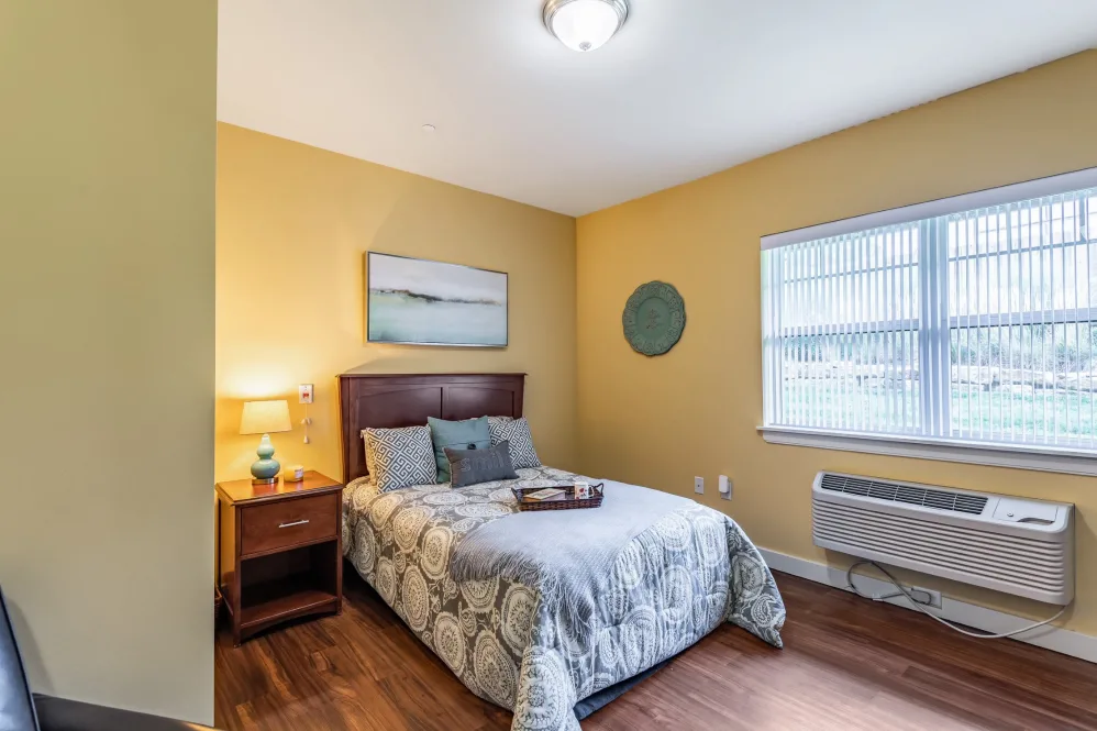 A cozy bedroom with a comfortable bed, nightstand, and window allowing natural light.
