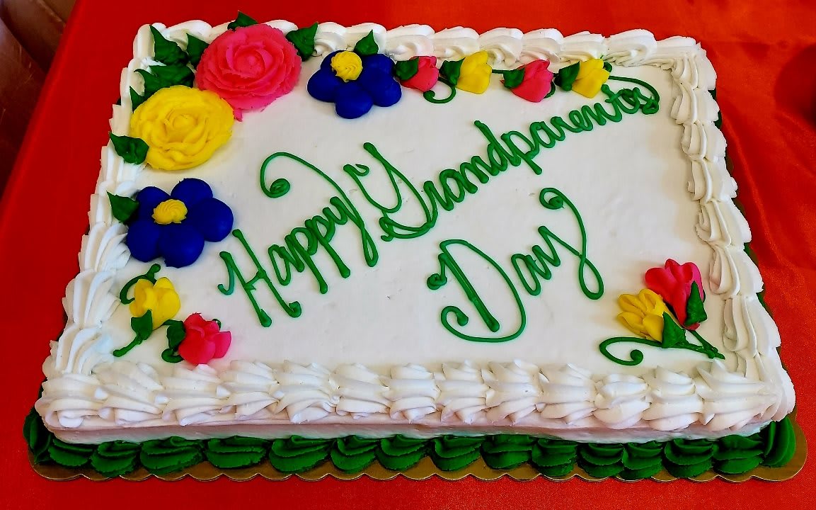 A festive cake decorated with colorful flowers and green icing, celebrating Grandparents Day.
