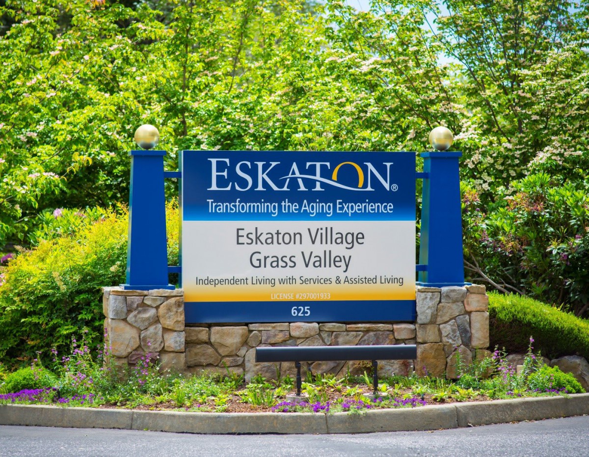 The entrance sign for Eskaton Village Grass Valley, featuring stone pillars and surrounded by greenery.