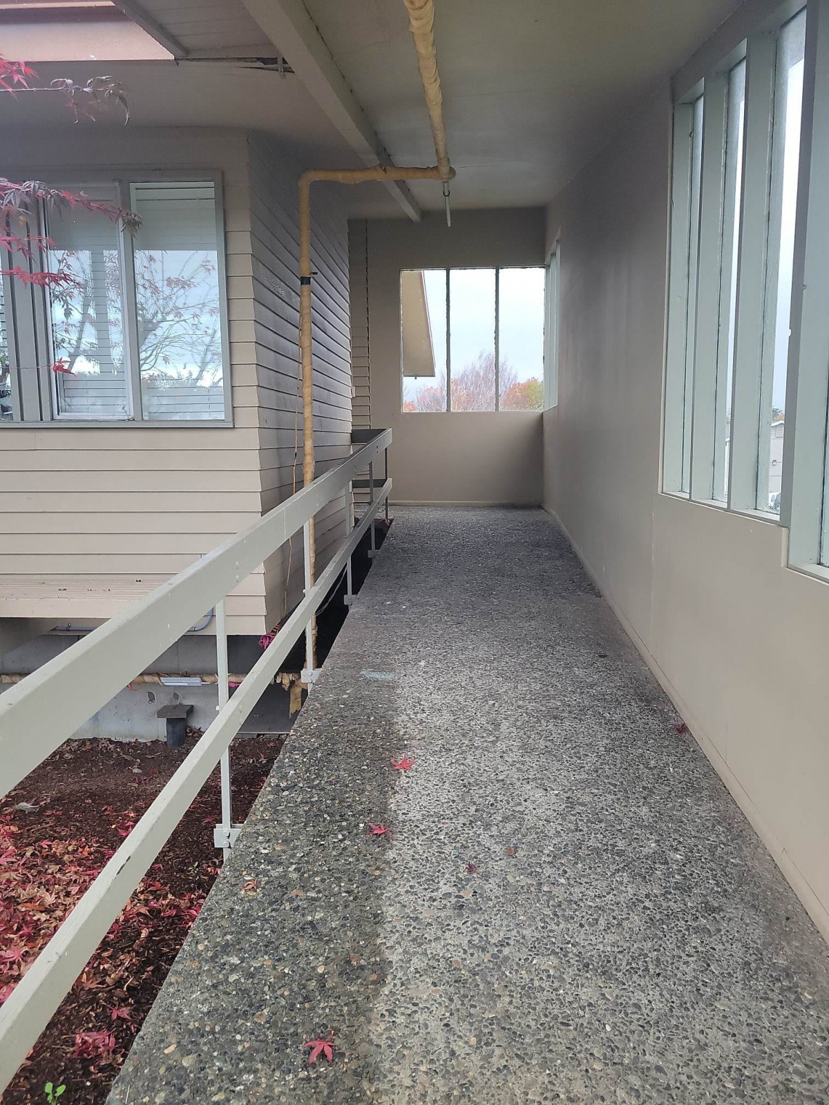 A covered outdoor hallway with windows on one side and a railing on the other.