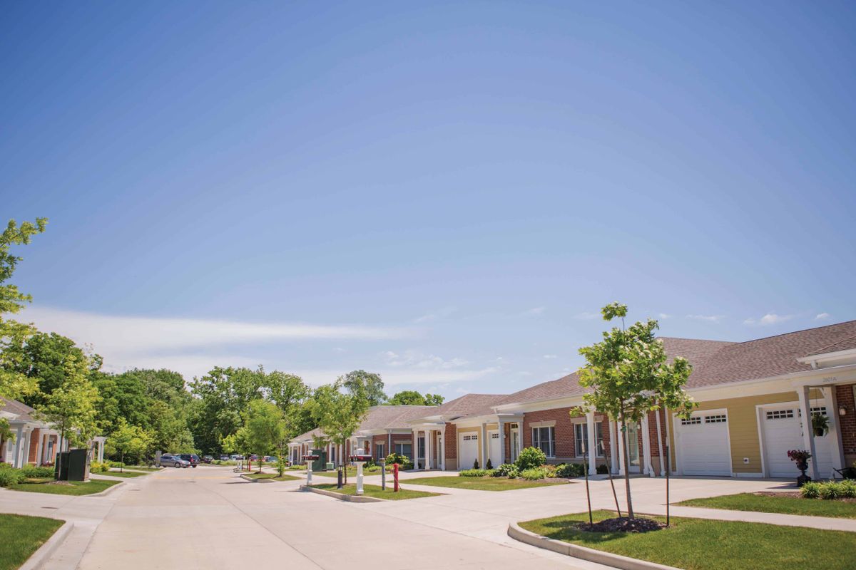 A peaceful suburban neighborhood with houses and trees lining the street under a clear blue sky.