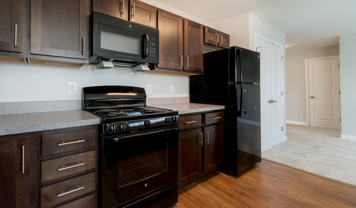 A modern kitchen featuring dark wood cabinets, a stove, microwave, and refrigerator.