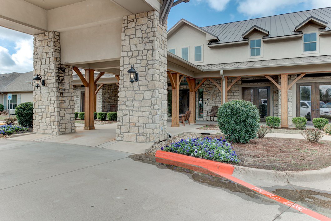 A stone building entrance with a landscaped garden and paved driveway.